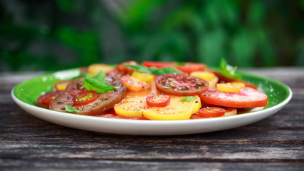 Colorful Tomato Salad with heirloom, pear shaped, beef heart, tigerella, brandywine, cherry, black tomatoes in a green plate. healthy food