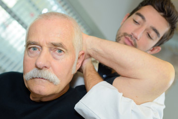 male physiotherapist examining the neck of an elderly man