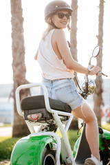 Young woman in safe bike helmet and protective glasses exercises in riding using electric bicycle...