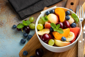 Bowl of healthy fresh fruit salad on a blue rusty background. Top view