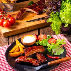 bbq spareribs on the plate with green salad and white sauce.