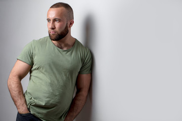 Isolated shot of handsome man with dark stubble, wears casual khaki t shirt, poses against white...
