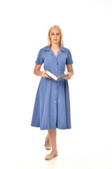 full length portrait of blonde girl wearing blue dress. standing pose holding a book. isolated on white  studio background.