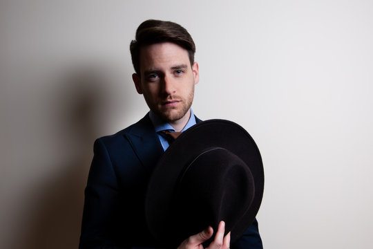 Portrait of a stylish handsome young man wear suit and holding a fedora hat in studio