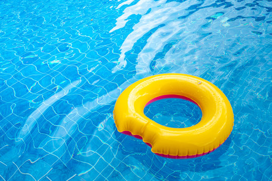 Sunny day at the pool.Bright yellow float in blue swimming pool, ring floating in a refreshing blue swimming pool with waves reflecting in the summer sun.Lifesaver for kid.
