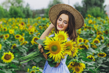 Young beautiful girl in dress and hat in field with sunflowers