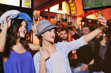 two cute young girlfriends in Bavarian hats smiling at the bar background during the celebration of the Oktoberfest