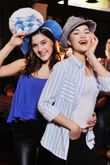 two cute young girlfriends in Bavarian hats smiling at the bar background during the celebration of the Oktoberfest