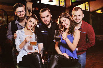 a group of friends - young guys and girls drinking beer, talking and smiling at the bar