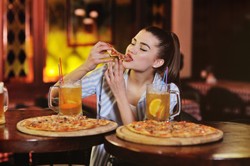 a young pretty girl eating pizza and drinking beer or a beer citrus cocktail on the background of a bar or pizzeria.