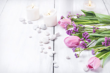 Pink flowers, white pebbles and burning candles on a white wooden background