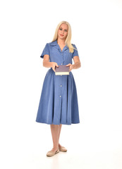 full length portrait of blonde girl wearing blue dress. standing pose holding a book. isolated on white  studio background.