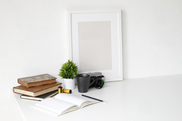 Work table with photography camera, book, notepad and pencil on white table and empty photo frame.