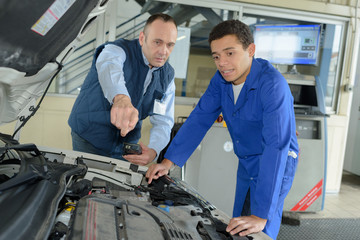 mechanic giving instructions to trainee looking at car engine