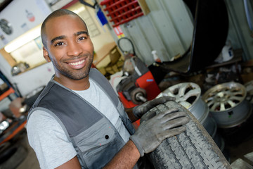 happy mechanic carrying a tire in tire service - obrazy, fototapety, plakaty
