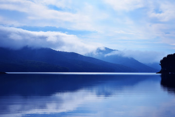 Dawn in the mountains. Morning fog over the sea. Reflection of clouds in the water. Early morning in the mountains. Mirror surface on the water.