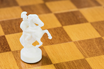 The isolated white chess knight of stone or plastic on the square wood board