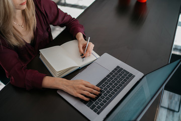 Fototapeta premium Female designer using laptop, sketching at blank notepad. Woman hand writing in notebook on wooden desk. Concept ease of use of Internet and accessibility of information of working process.