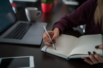 Close up view of female person with pen in hand writing notes in paper notepad taking them from internet. Selective focus on open notebook, student preparing for exam recording information from networ