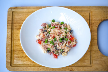 Italian rice salad or cold rice in a white plate on a chopping board with blurred white background.