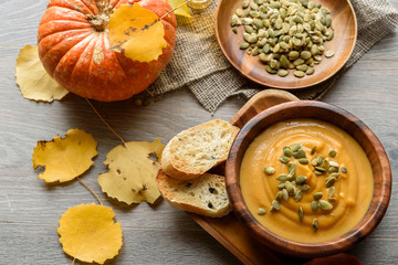 Pumpkin soup in a wooden bowl, with autumn leaves and pumpkin