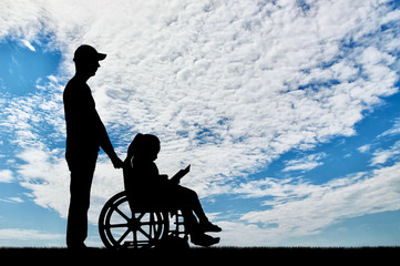Fototapeta na wymiar A disabled girl in a wheelchair and her dad on a walk reading a book