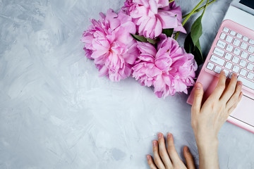 Feminine business mockup with peonies bouquet and woman's printing on pink laptop, flatlay on cement background with copyspace