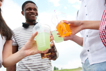 Close-up of teenagers holding plastic glasses with cocktails and toasting, they celebrating something