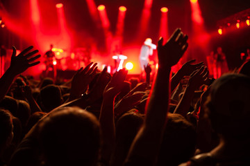 concert crowd during festival, hands of many people cheering musicians playing music on stage, red...