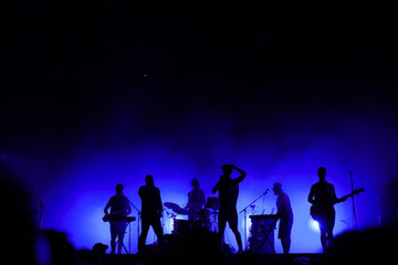 music band playing on concert stage, silhouettes of musicians unrecognizable, group of people singing together in rock festival