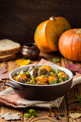 Beef stew with pumpkin, peas and thick sauce, autumn food. Dark bowl on wooden background in rustic style