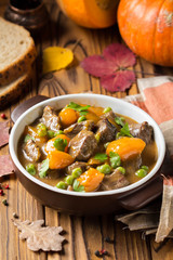 Beef stew with pumpkin, peas and thick sauce, autumn food. Dark bowl on wooden background in rustic style