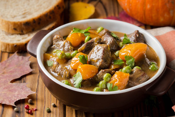 Beef stew with pumpkin, peas and thick sauce, autumn food. Dark bowl on wooden background in rustic style