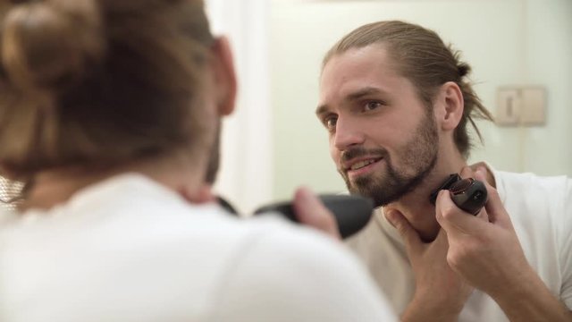 Man Shaving Face With Trimmer Looking In Mirror
