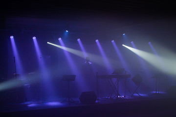 Bühne mit viel Nebel und effektvollem Licht und einer nicht erkennbaren Person auf der Bühne mit Instrumenten und Technik