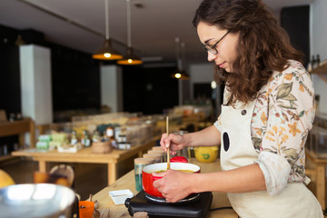 Beautiful woman standing by the stove in the kitchen, cooking and smelling the nice aromas from her meal in a pot in organic store