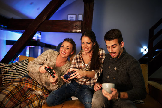 Group of best friends sitting at home on pleasant evening and playing games on console.They challenge each other to win .
