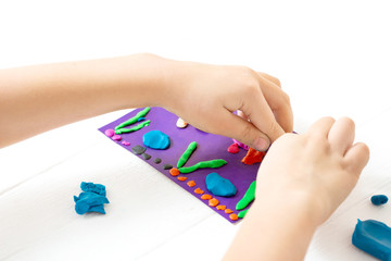 A child kneads plasticine and sculpts an aquarium with fish. Tutoring with children