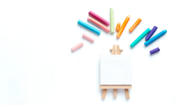 A small malbert with a clean canvas on a white background surrounded by colorful crayons. Template