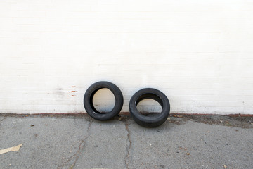Two car tires leaning on a white wall