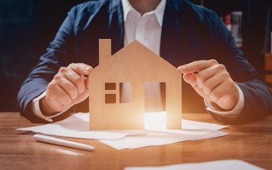Man proposing signing a estate insurance policy, the agent is holding the wooden house model. Estate insurance concept.