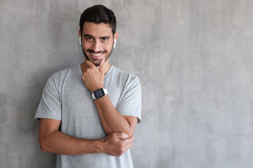 Portrait of handsome man in t shirt, standing against gray textured wall with copy space for your ads, showing his stylish modern smart watch with empty screen
