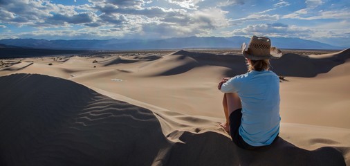 Woman in hat looking out over the Mesquite Flat Sand Dunes in Death Valley National Park at sunset - obrazy, fototapety, plakaty