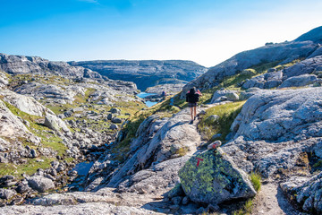 Fototapeta na wymiar Hiker on the trail around Lysefjord, Norway. Water, cliffs and rocks are all around.