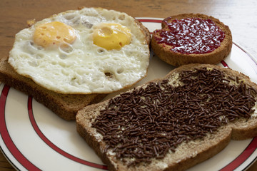 a breakfast with well done eggs, chocolate milk sprinkles and raspberry jam on brown slices of bread on a plate