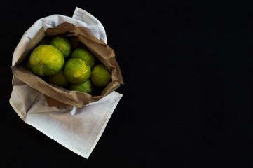 Overhead view of a recycled paper bag with organic fig fruits on unpolluted white fabric. Dark still life scene with black and elegant background.