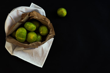 Overhead view of a recycled paper bag with organic fig fruits on unpolluted white fabric. Dark still life scene with black and elegant background.