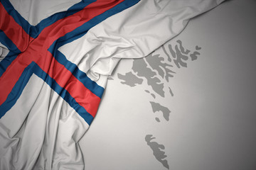 waving colorful national flag and map of faroe islands.
