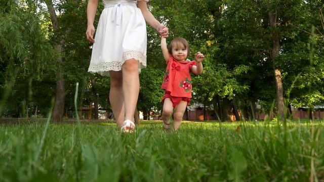 child and mother walk on green lawn grass in summer city Park and smiling.