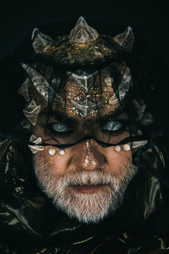 Demon with golden skin, thorns on faceand grey beard giding under dark veil. Portrait of man with fictional makeup on black background, fantasy concept